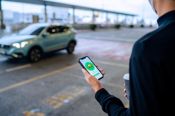Pasajero solicitando un viaje compartido en su teléfono mientras un auto se acerca