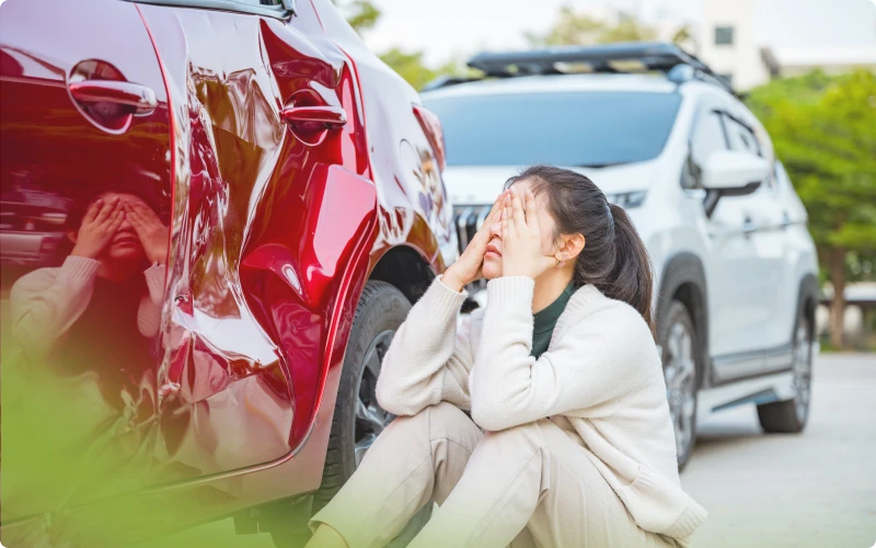 Mujer angustiada sentada junto a su auto dañado tras un accidente