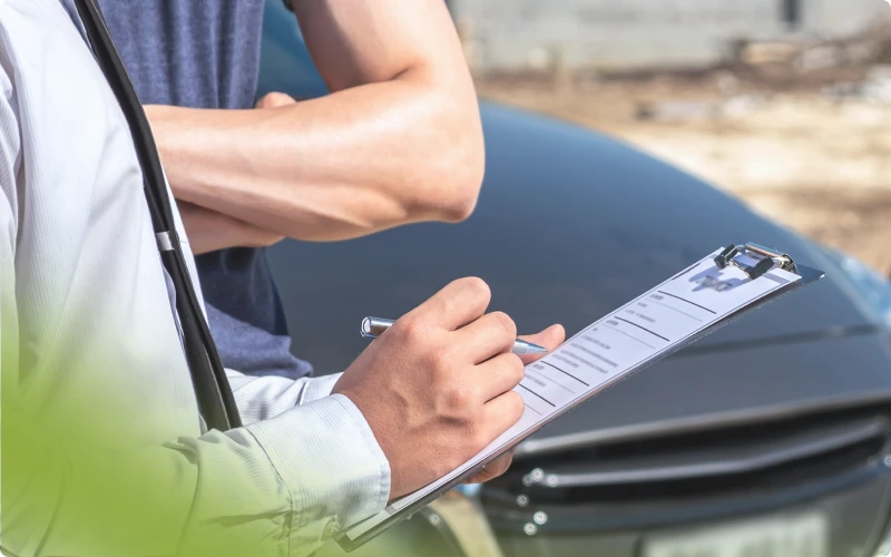 Persona anotando en un formulario junto a un auto dañado