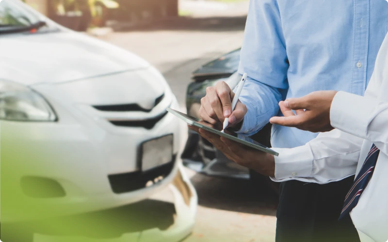 Ajustador de seguros tomando notas en una tableta junto a autos chocados