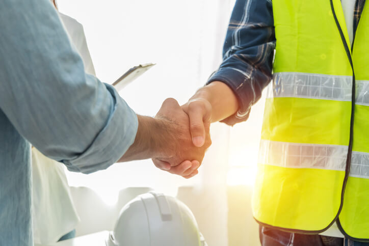 Trabajador de la construcción y abogado se dan la mano junto a un casco de seguridad