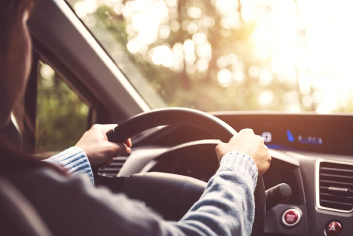 Vista del conductor con las manos en el volante durante un trayecto al atardecer